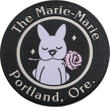 Circular challenge coin featuring a French Bulldog holding a pink rose with 'The Marie-Marie' and 'Portland, Ore.' text.