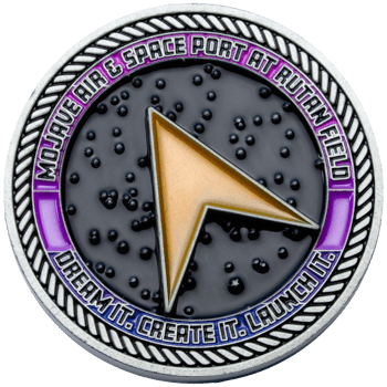 Round challenge coin for Mojave Air & Space Port at Rutan Field featuring a gold delta symbol against a black starry background and a purple outer ring.