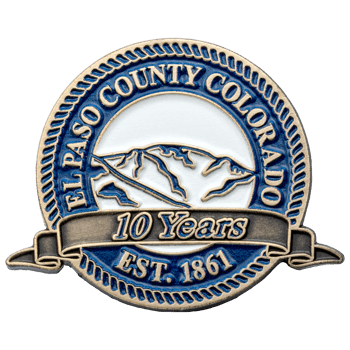 Circular lapel pin for El Paso County Colorado featuring a mountain range, blue border, and 10 Years Est. 1861 banner.