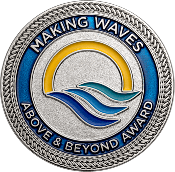 Silver-toned challenge coin with blue and yellow enamel featuring waves and a sun graphic, bordered by rope edging.