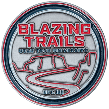 Circular silver challenge coin featuring Blazing Trails Utah Tech University text and a red-outlined mountain landscape design.