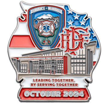 Shield-shaped challenge coin featuring the Frederick-Firestone Fire District logo, a fire station illustration, and American flag background.