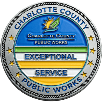 Silver challenge coin for Charlotte County Public Works with sun and leaf logo, rope edge, and text for Exceptional Service.