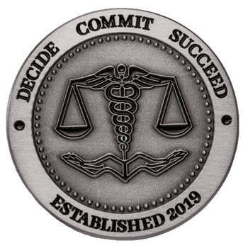 Circular brushed silver medallion featuring a caduceus, scales of justice, and hands, with text reading Decide Commit Succeed Established 2019.