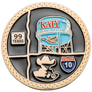 Round challenge coin featuring a blue water tower with Katy text, a goose, Texas 99 and Interstate 10 signs, and a cowboy silhouette on a black background.